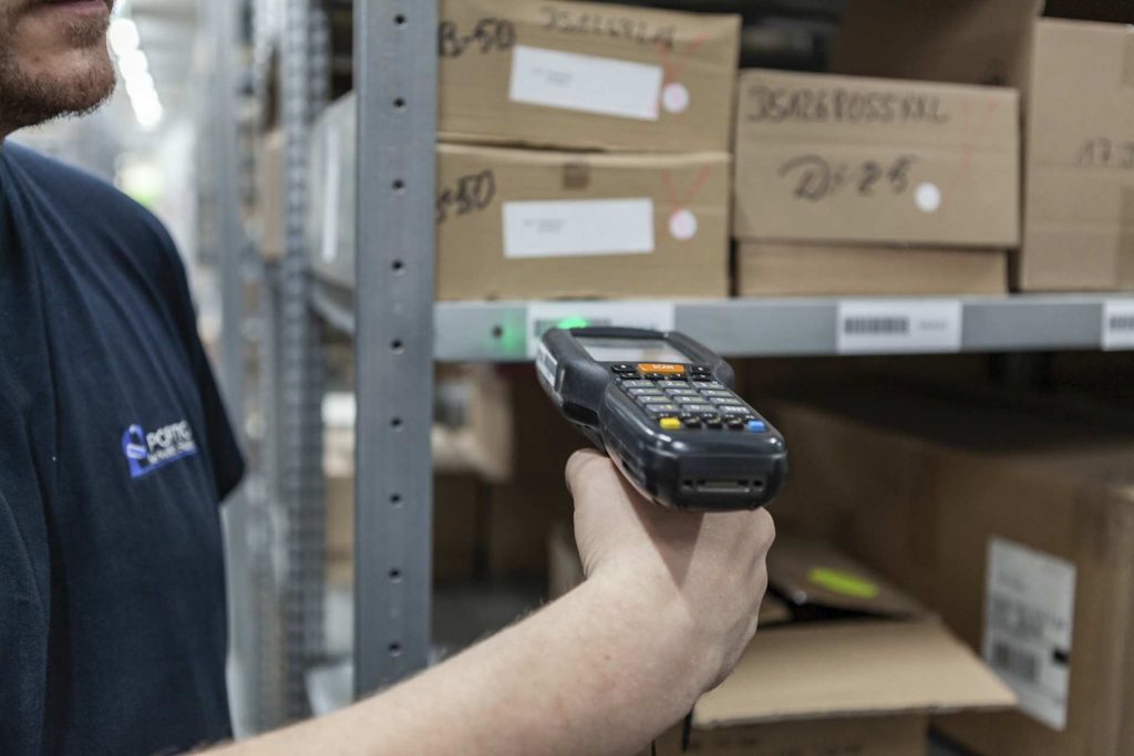 Mitarbeiter scannt Barcode mit mobilem Scanner im Lager vor Kartonregalen
