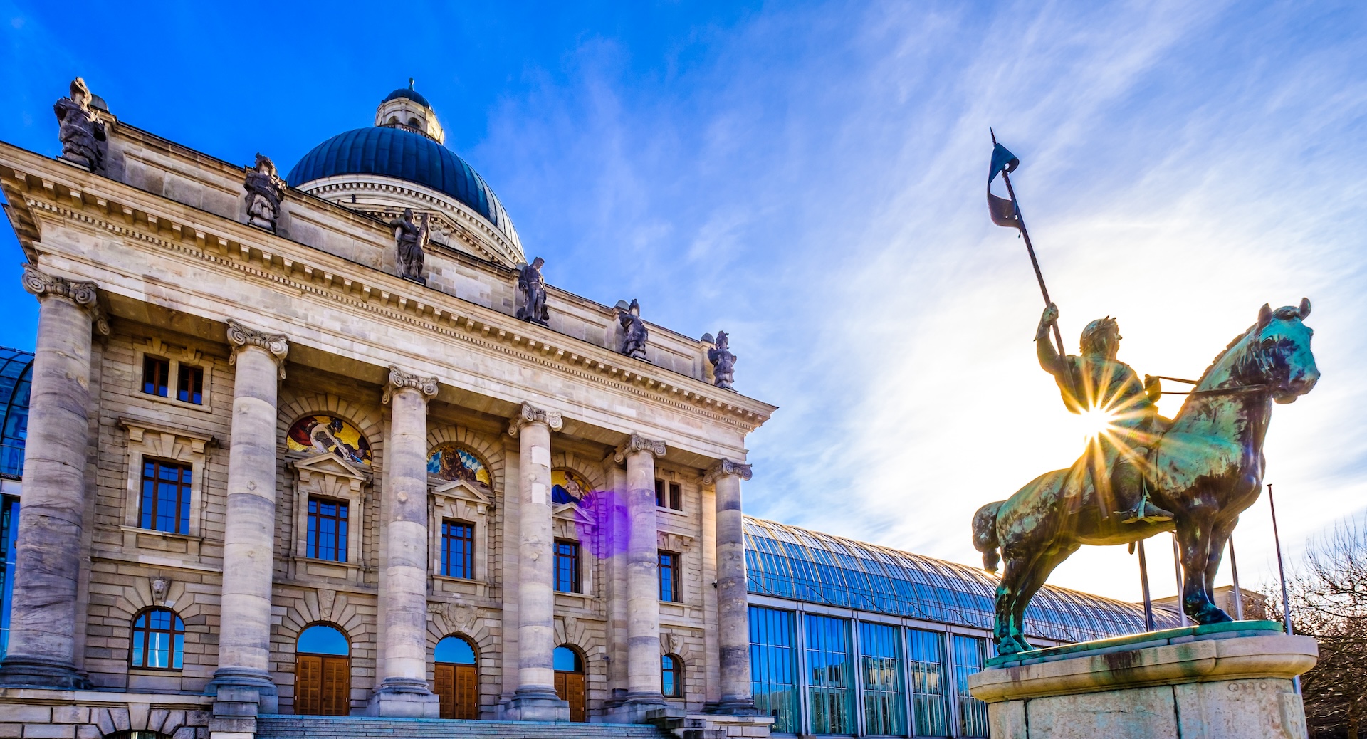 Bayerische Staatskanzlei München mit neoklassizistischer Fassade, blauer Kuppel und Reiterstatue bei Sonnenschein