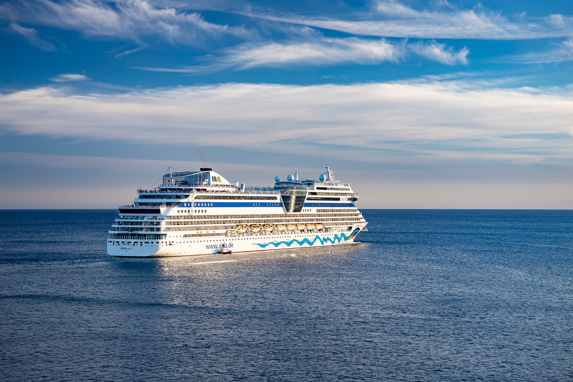 Weißes AIDA Kreuzfahrtschiff mit türkisem Wellendesign fährt auf blauem Meer unter bewölktem Himmel