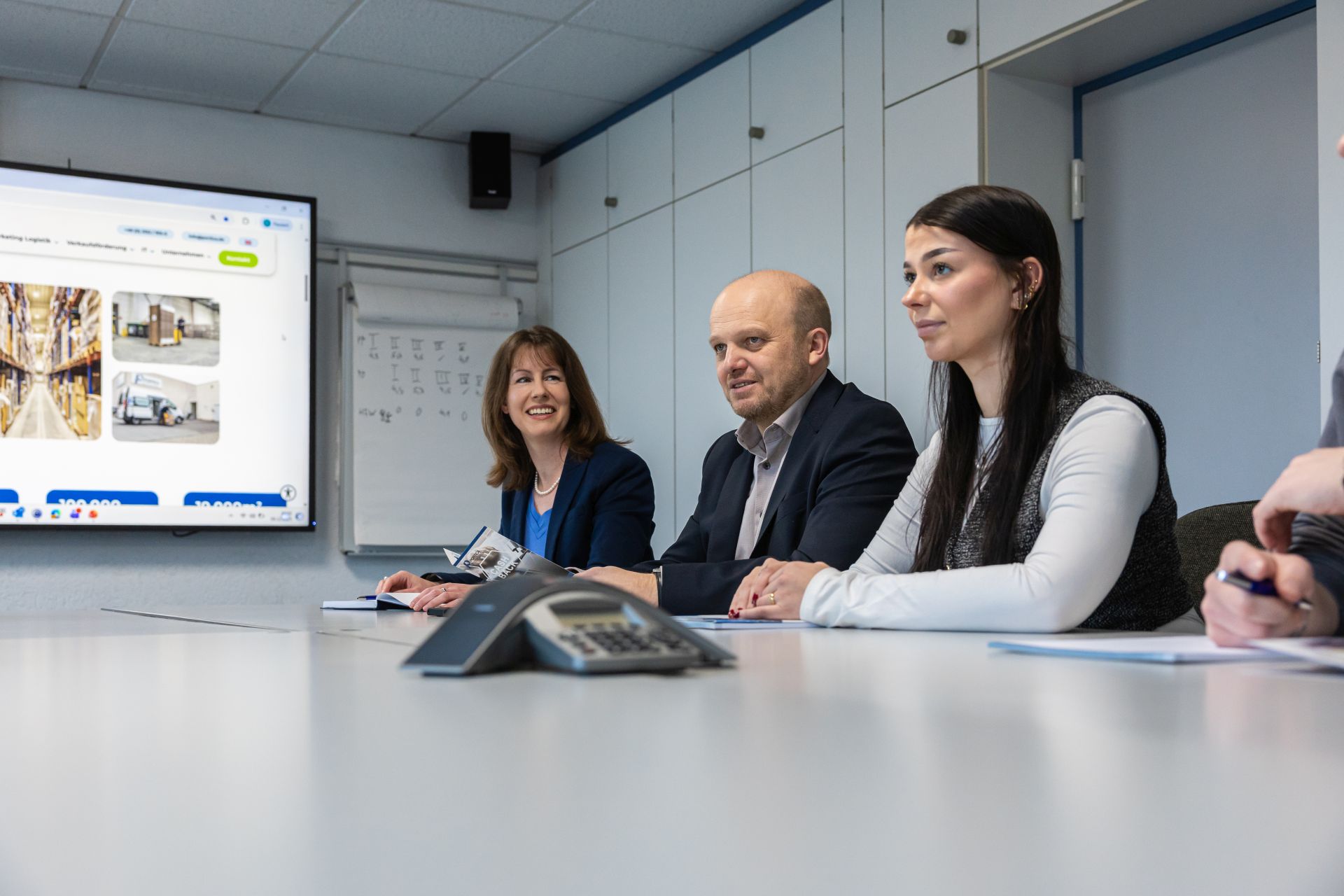 Drei Geschäftsleute in Besprechung am Konferenztisch mit Projektor und Whiteboard im modernen Büroraum