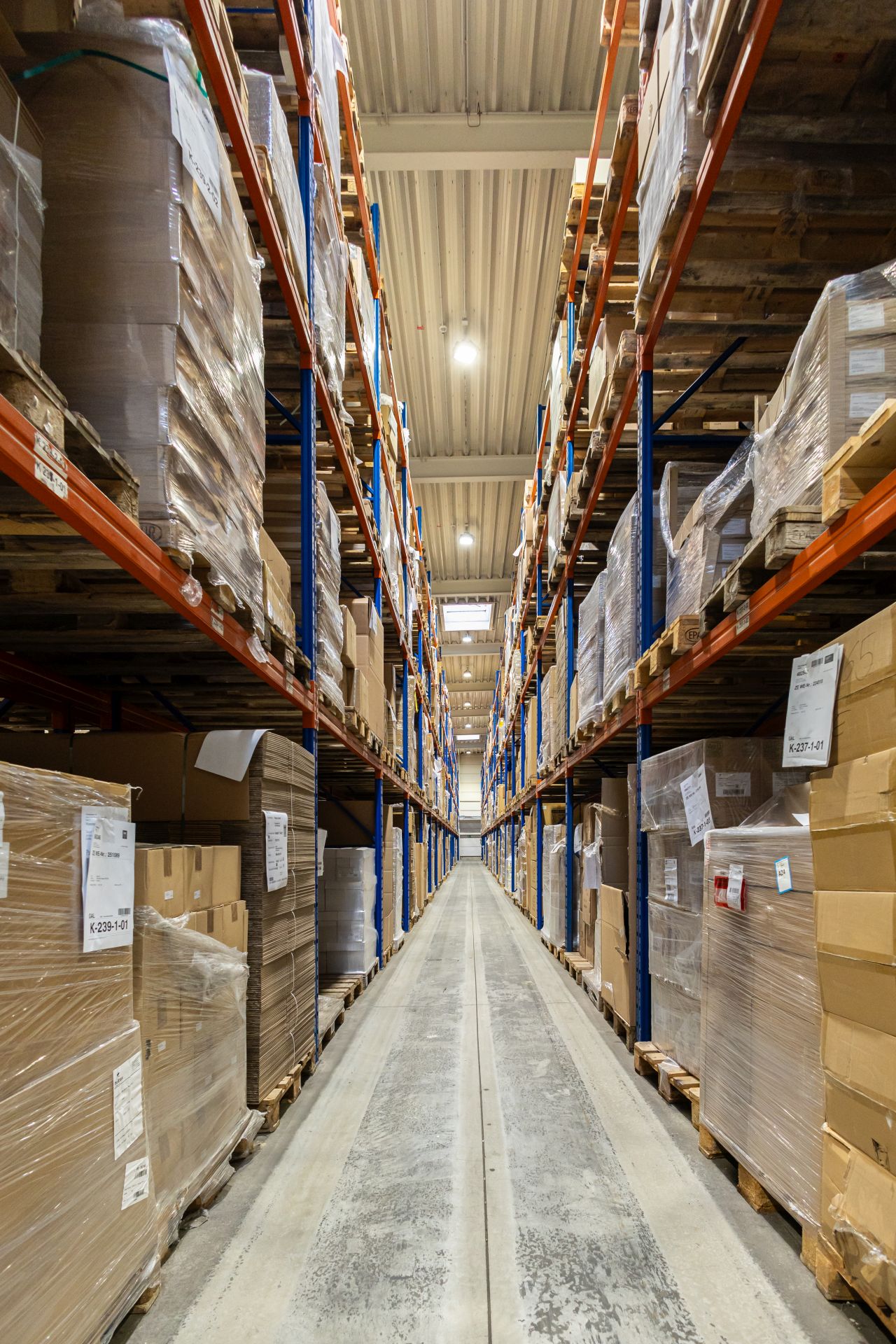 Langer Gang zwischen hohen Lagerregalen mit verpackten Kartons und Paletten in einem Logistikzentrum